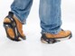 Mise en situation des crampons noir à 24 griffes métalliques Semptec sur les baskets brunes d'une personne en jean marchant dans la neige