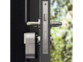 Mécanisme de serrure de porte motorisé et connecté coloris gris métal installé sur une porte d'entrée ouverte sur l'extérieur